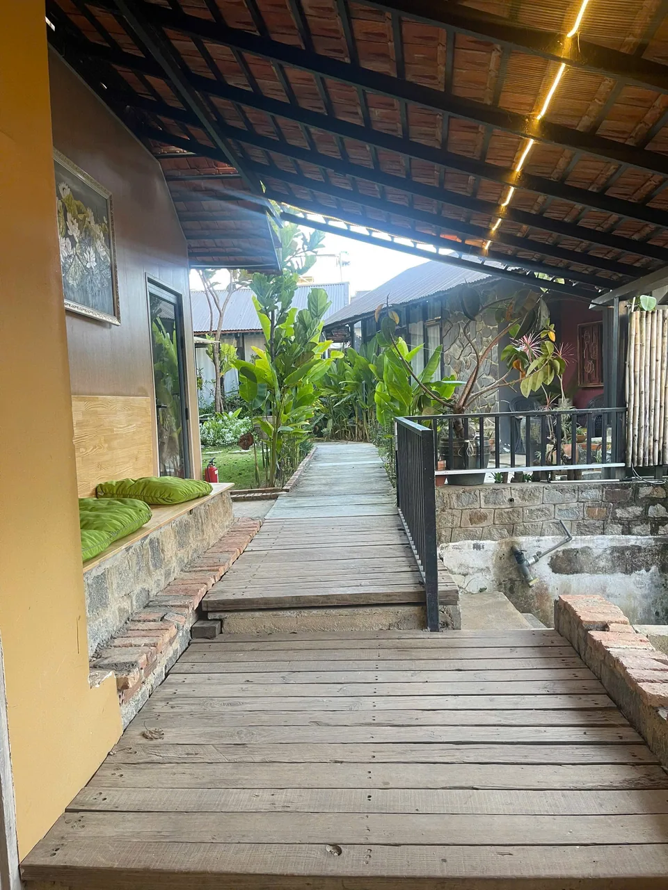 Hành lang gỗ dẫn vào các phòng trị liệu, đệm ngồi xanh và đèn vàng dưới mái ngói